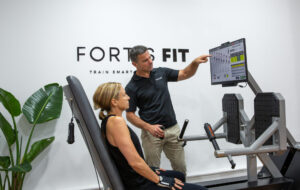 Personal trainer assisting a client with using the ARX adaptive resistance machine at Fortis Fit Personal Training in Sydney. Biohacking facility, ewot, red light therapy, carol bike, biocharger.